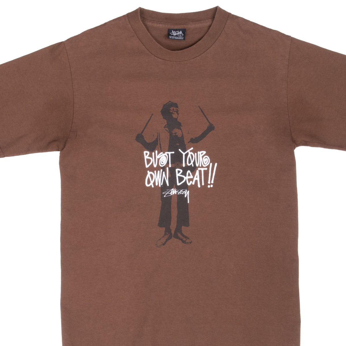 Front close-up of brown Stussy T-shirt with drummer figure and white Bust Your Own Beat lettering