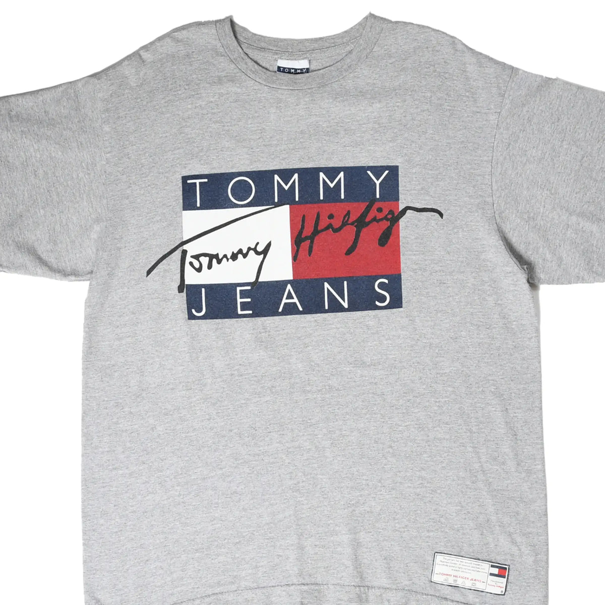 Front close-up of grey Tommy Jeans T-shirt with navy, white and red spellout graphic and hem label