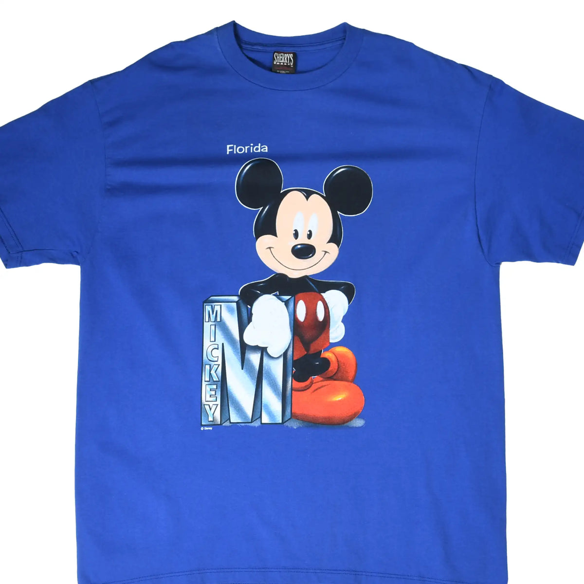 Front of blue T-shirt with Florida Mickey Mouse graphic leaning on a large letter M