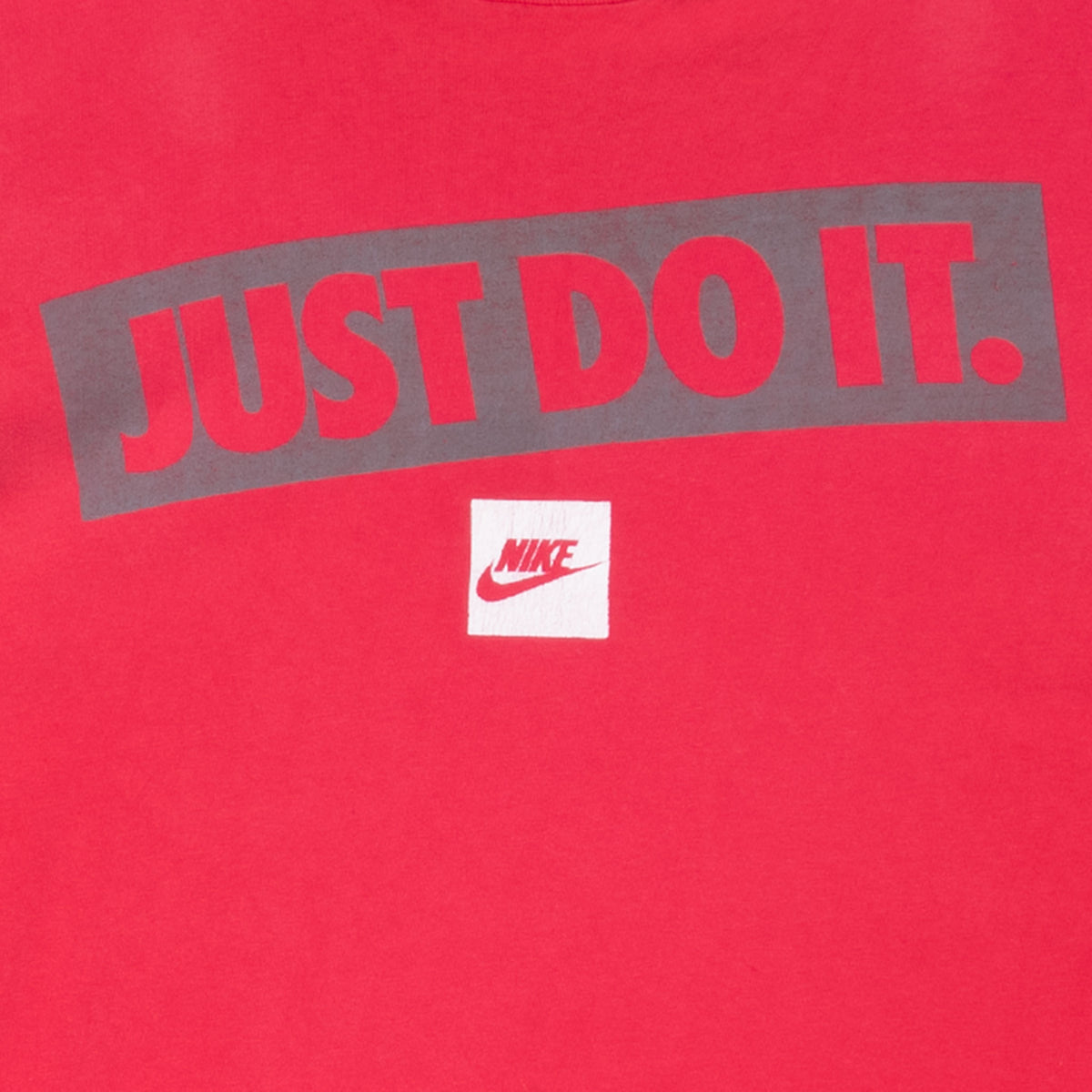 Close-up of gray Just Do It chest print and Nike Swoosh patch on red T-shirt