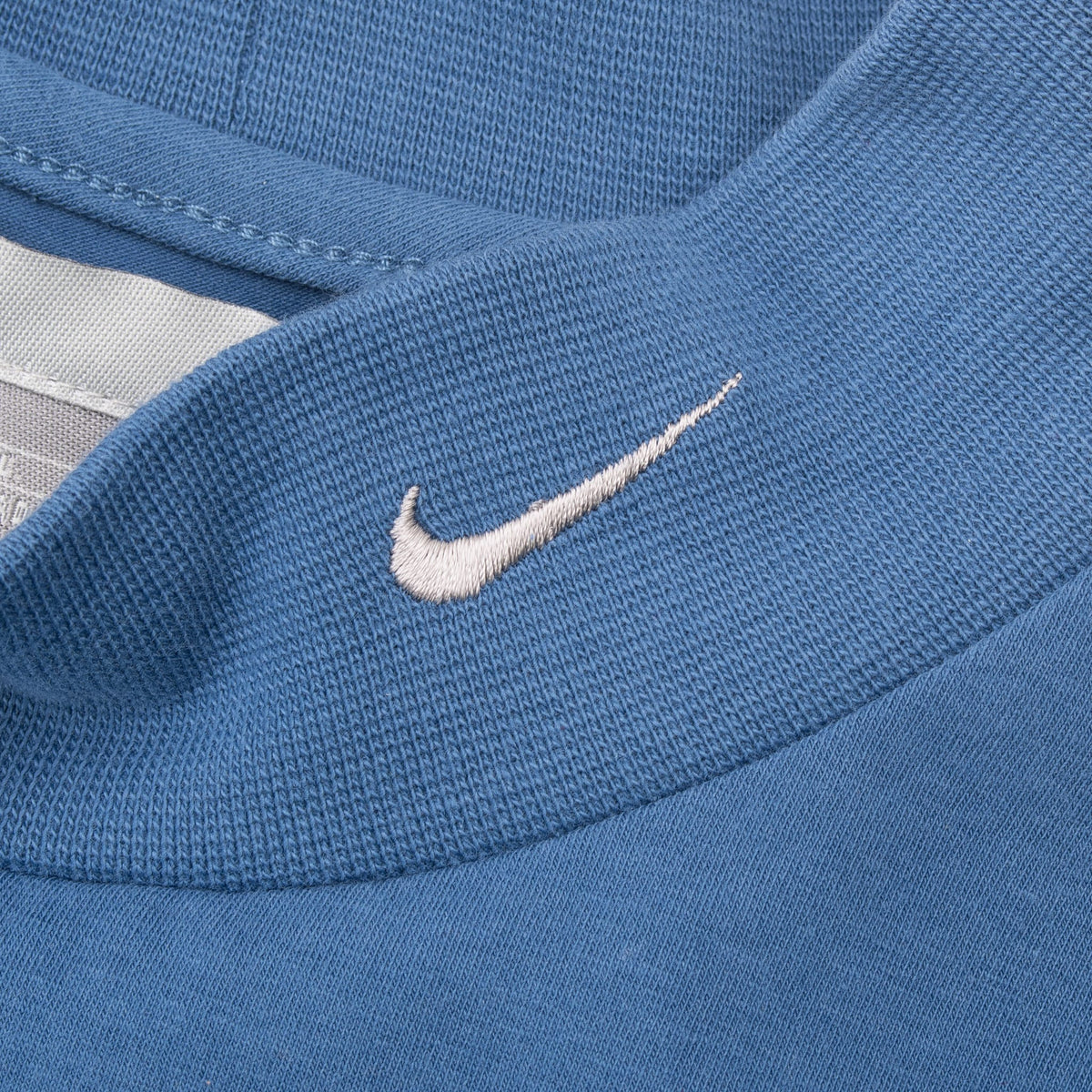 Close-up of white embroidered Nike Swoosh on blue turtleneck collar