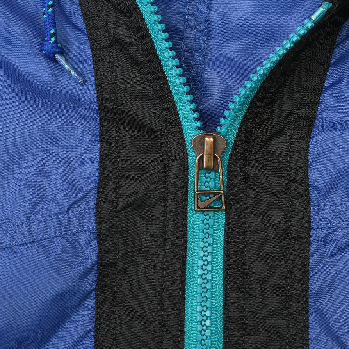 Close-up of teal front zipper and Nike Swoosh zipper pull on blue and black windbreaker