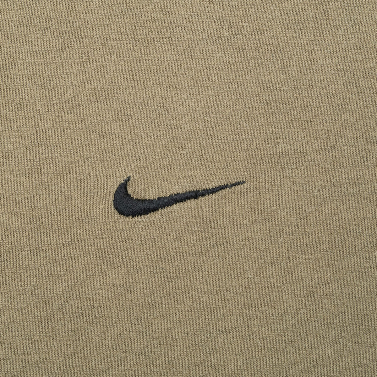 Close-up of black embroidered Nike Swoosh on khaki green fabric