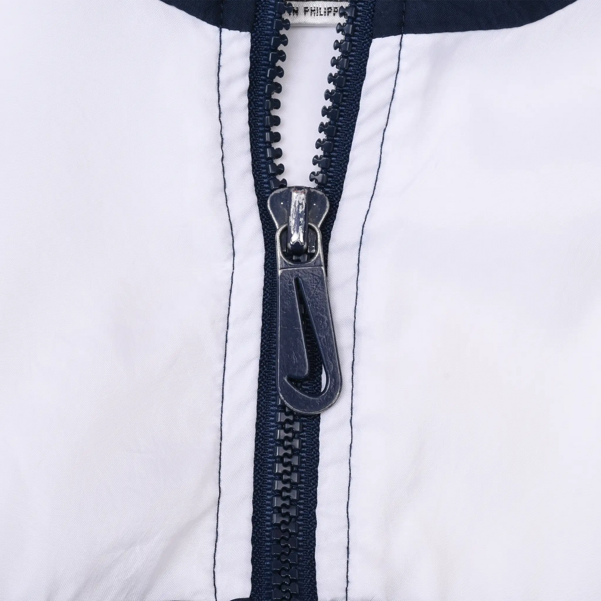Close-up of navy front zipper and Nike Swoosh pull on white fabric