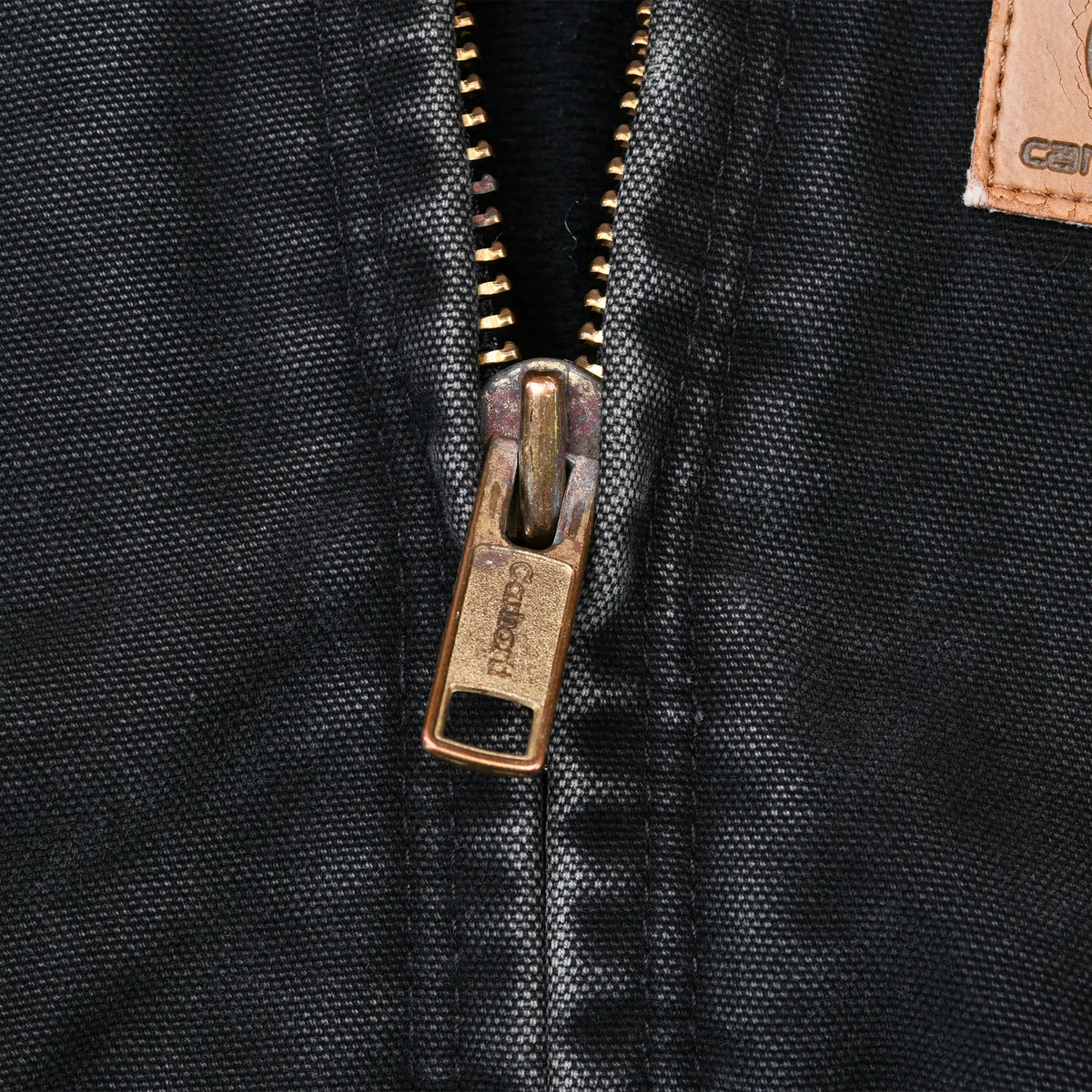 Close-up of brass Carhartt zipper on black jacket fabric