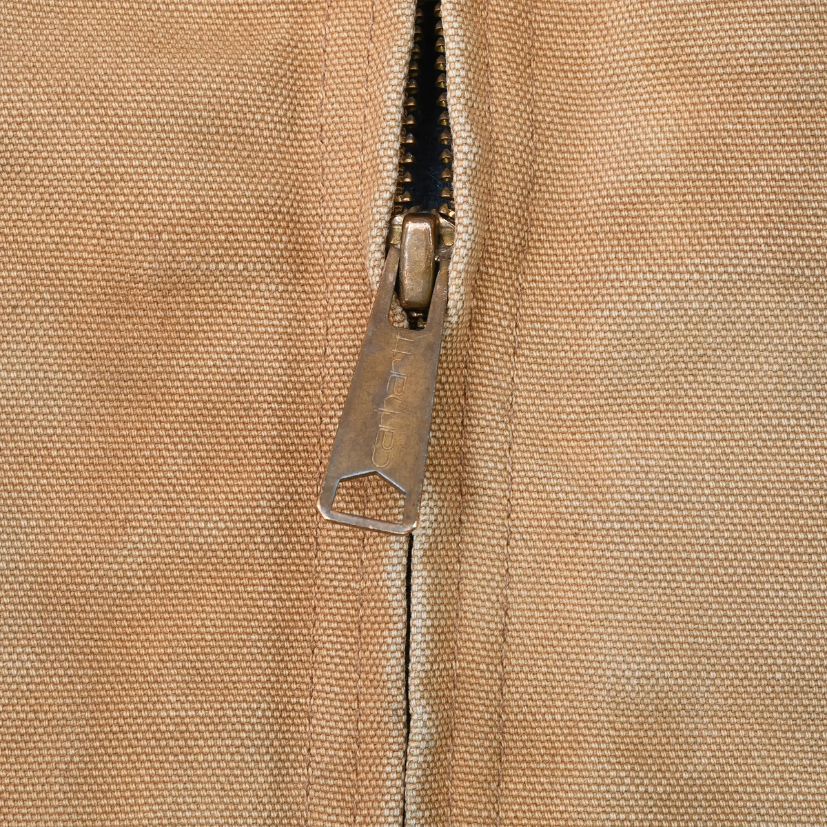 Close-up of metal Carhartt zipper pull on brown jacket fabric