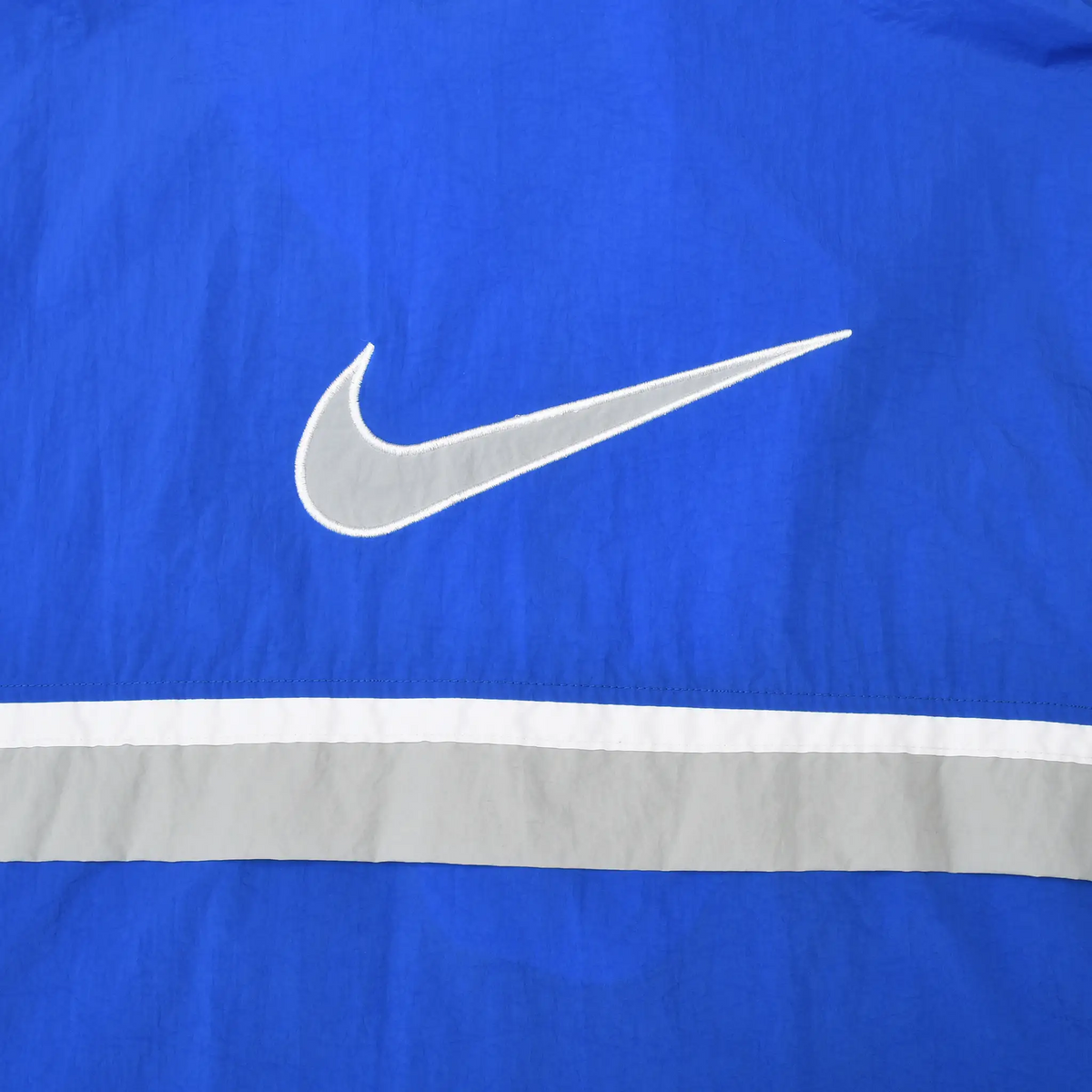 Close-up of large white Nike Swoosh embroidery and stripe on blue jacket back