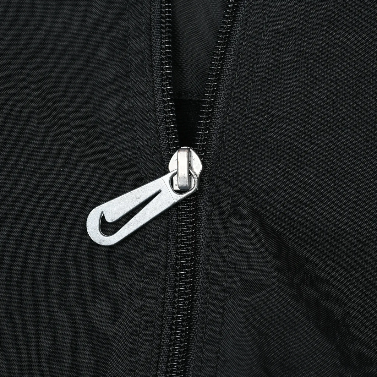 Close-up of silver Nike Swoosh zipper pull on black windbreaker jacket
