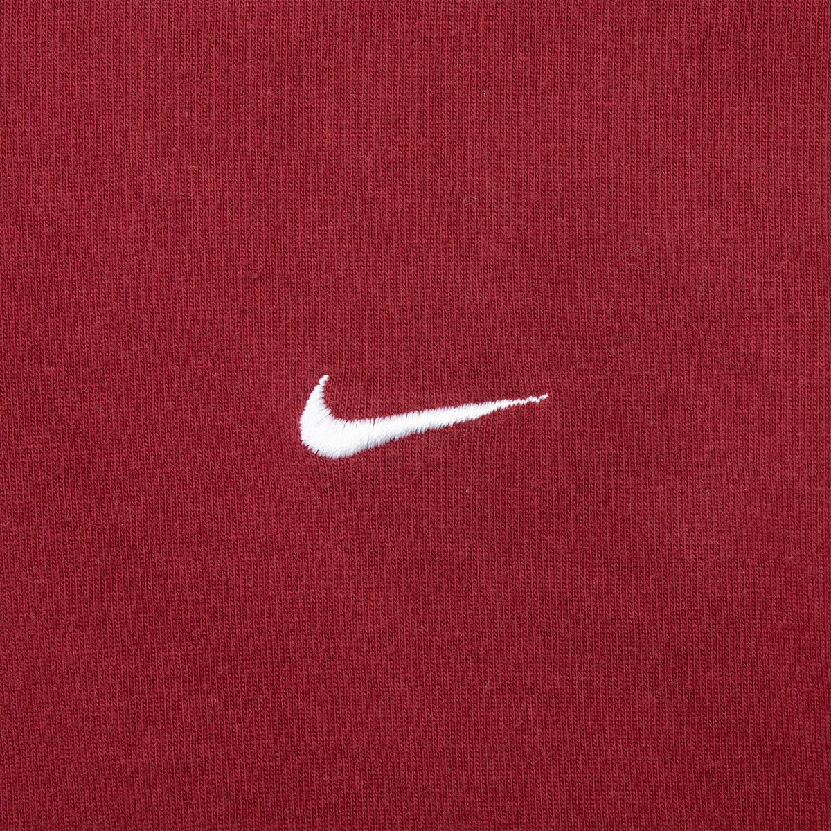 Close-up of white Nike Swoosh embroidery on burgundy fabric