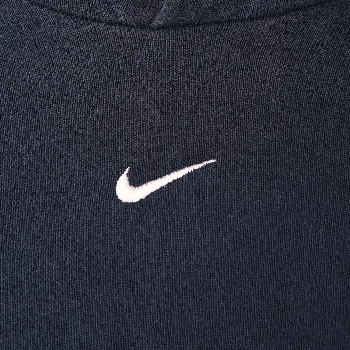 Close-up of white Nike Swoosh embroidery centered on navy blue hoodie chest