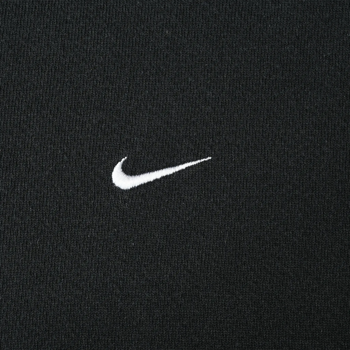 Close-up of small white Nike Swoosh embroidery on black fabric