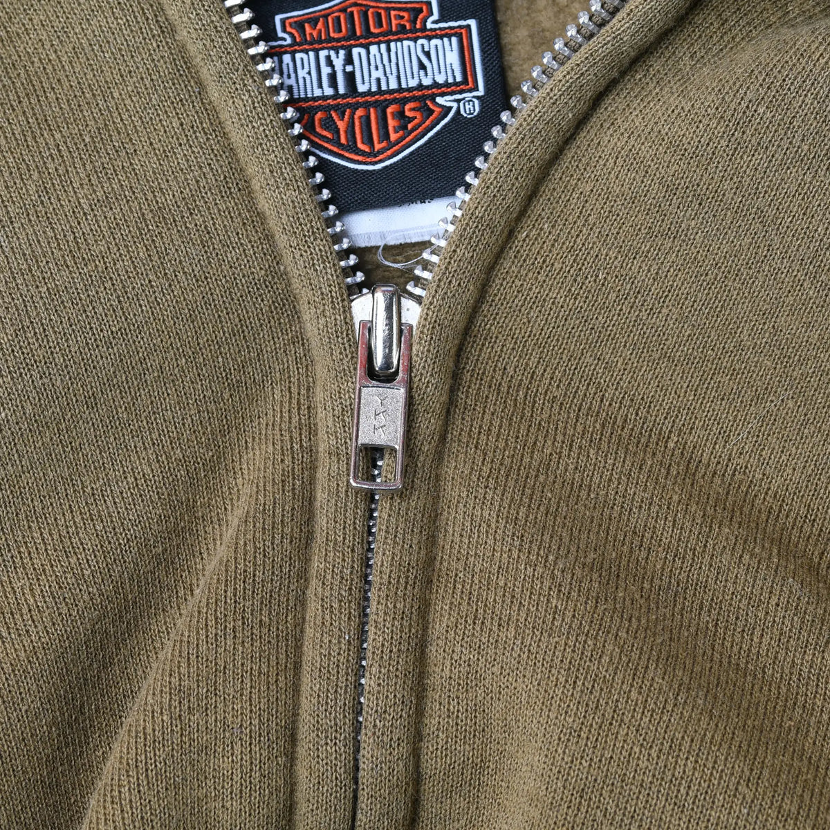 Close-up of metal zipper, khaki green fabric, and Harley-Davidson neck label