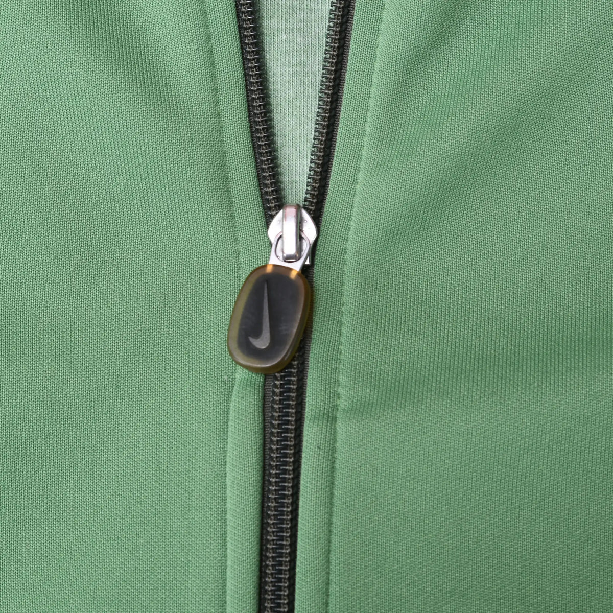 Close-up of black front zipper and oval pull on green Nike track jacket