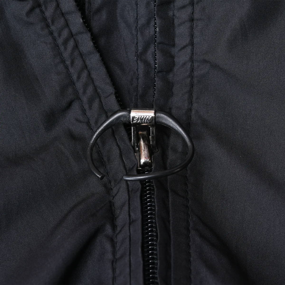 Close-up of the Nike jacket's black front zipper pull with oval cord loop