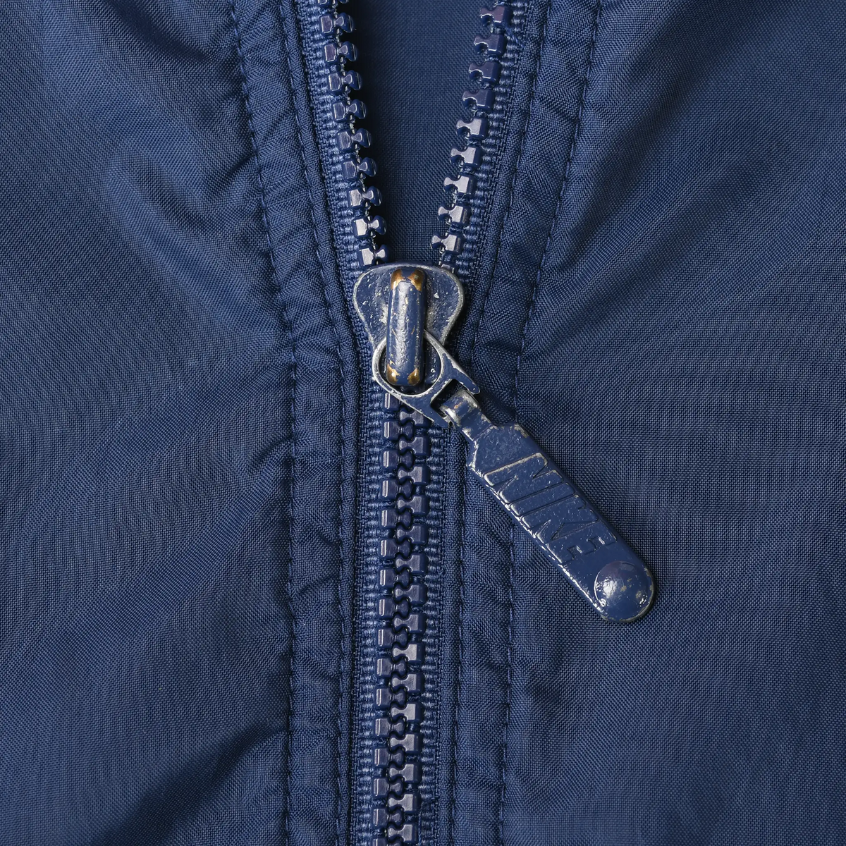 Close-up of the navy windbreaker's front zipper and metal pull