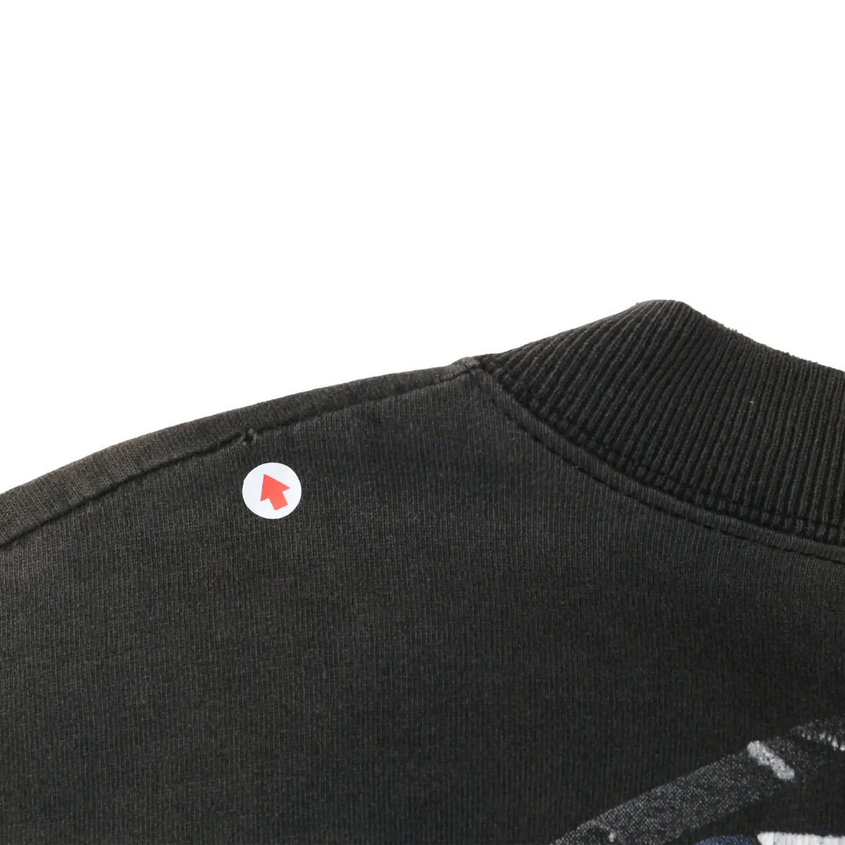 Close-up of black tee shoulder seam and ribbed collar with a small spot marked by an arrow
