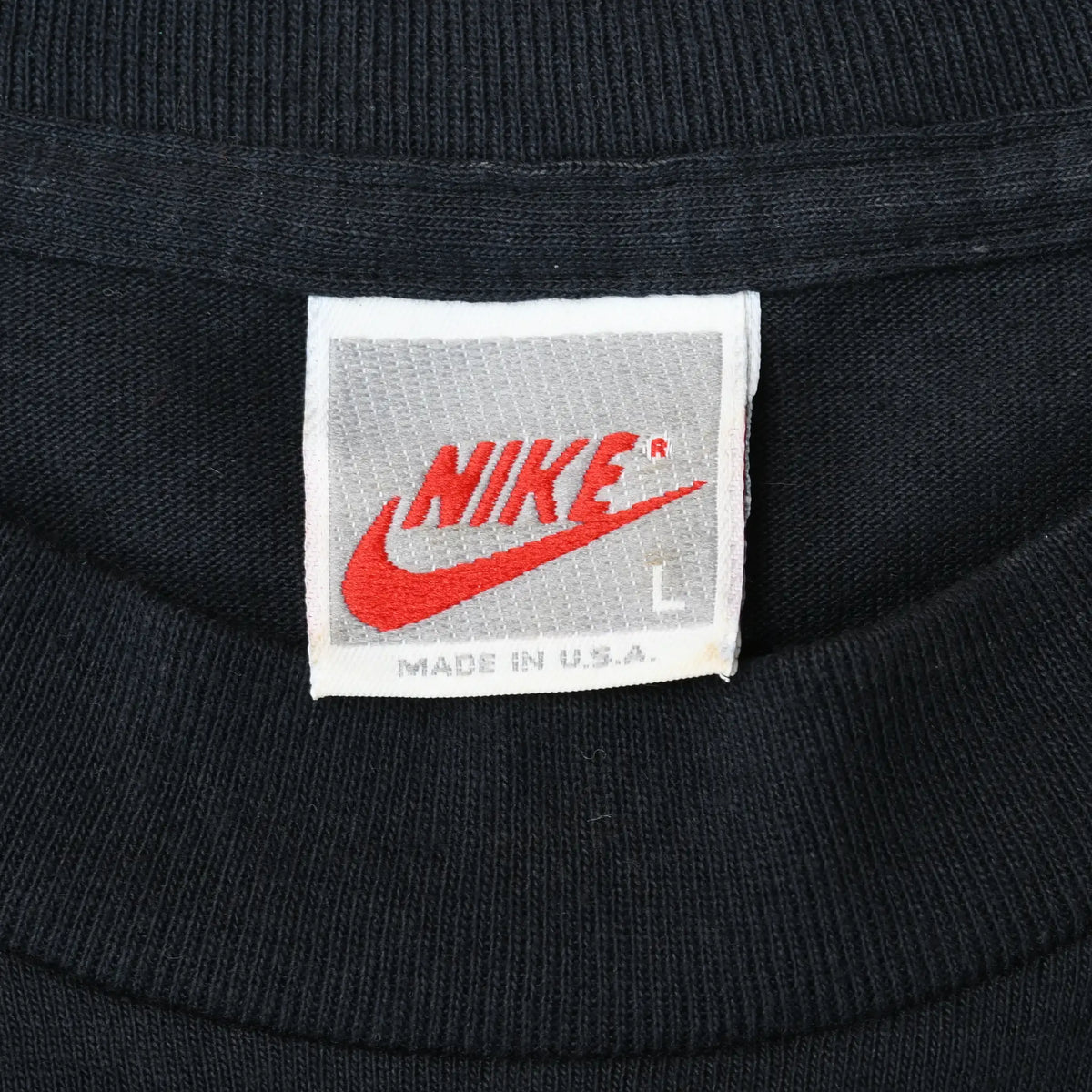 Close-up of white Nike neck tag marked L and Made in U.S.A. inside black T-shirt