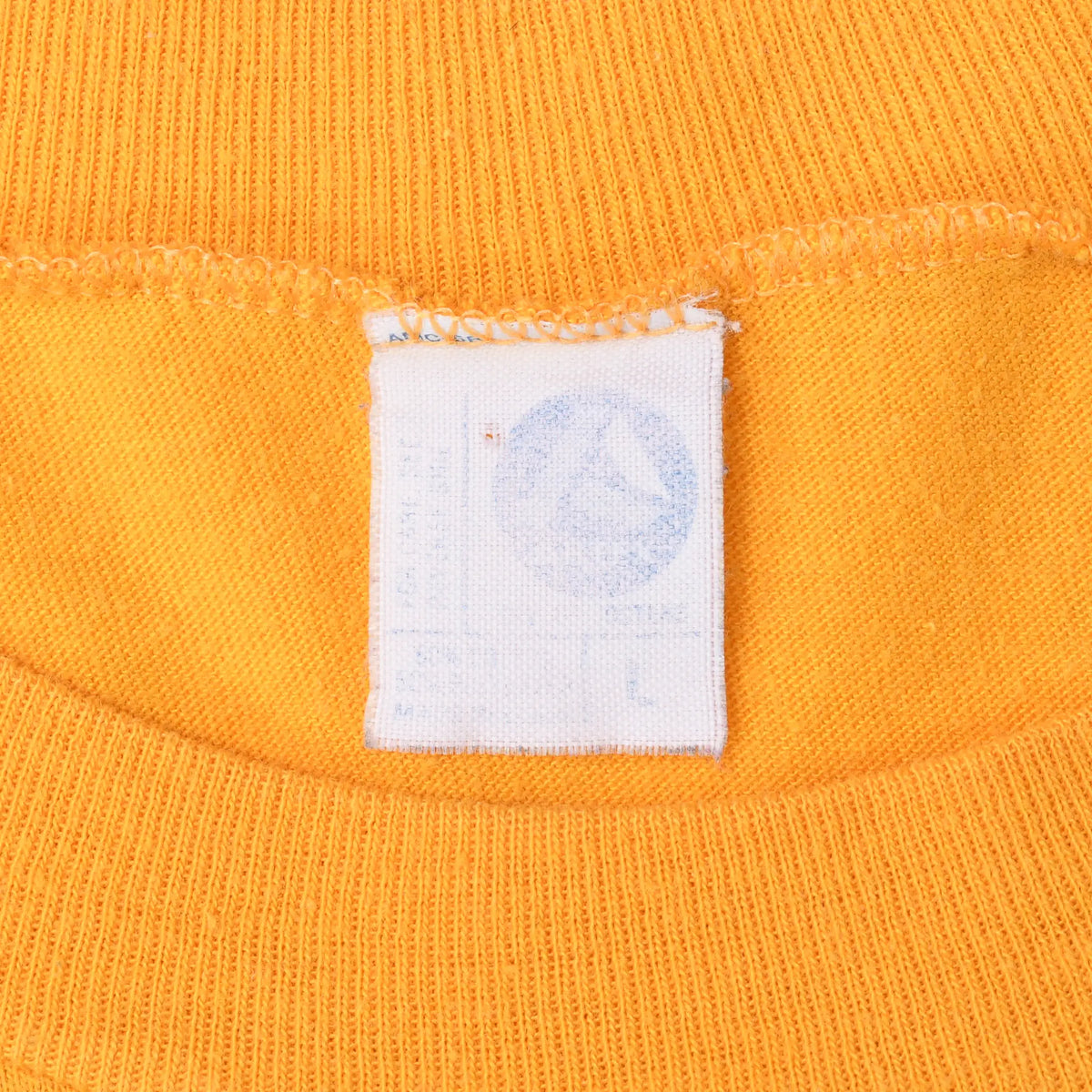 Close-up of faded white neck tag and ribbed collar on gold T-shirt