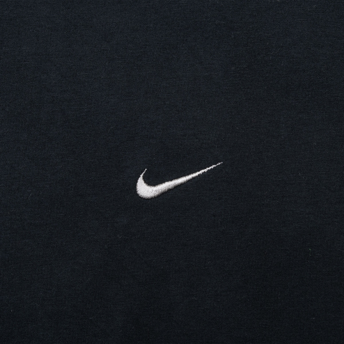 Close-up of small white Nike Swoosh embroidery on black fabric