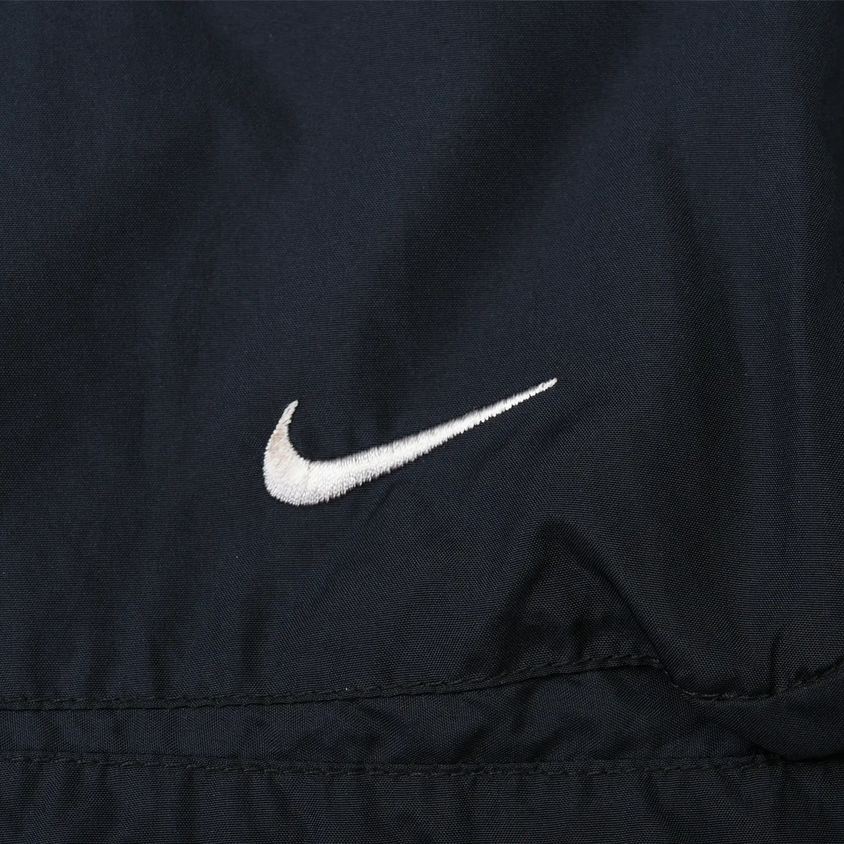 Close-up of white Nike Swoosh embroidery on black windbreaker fabric