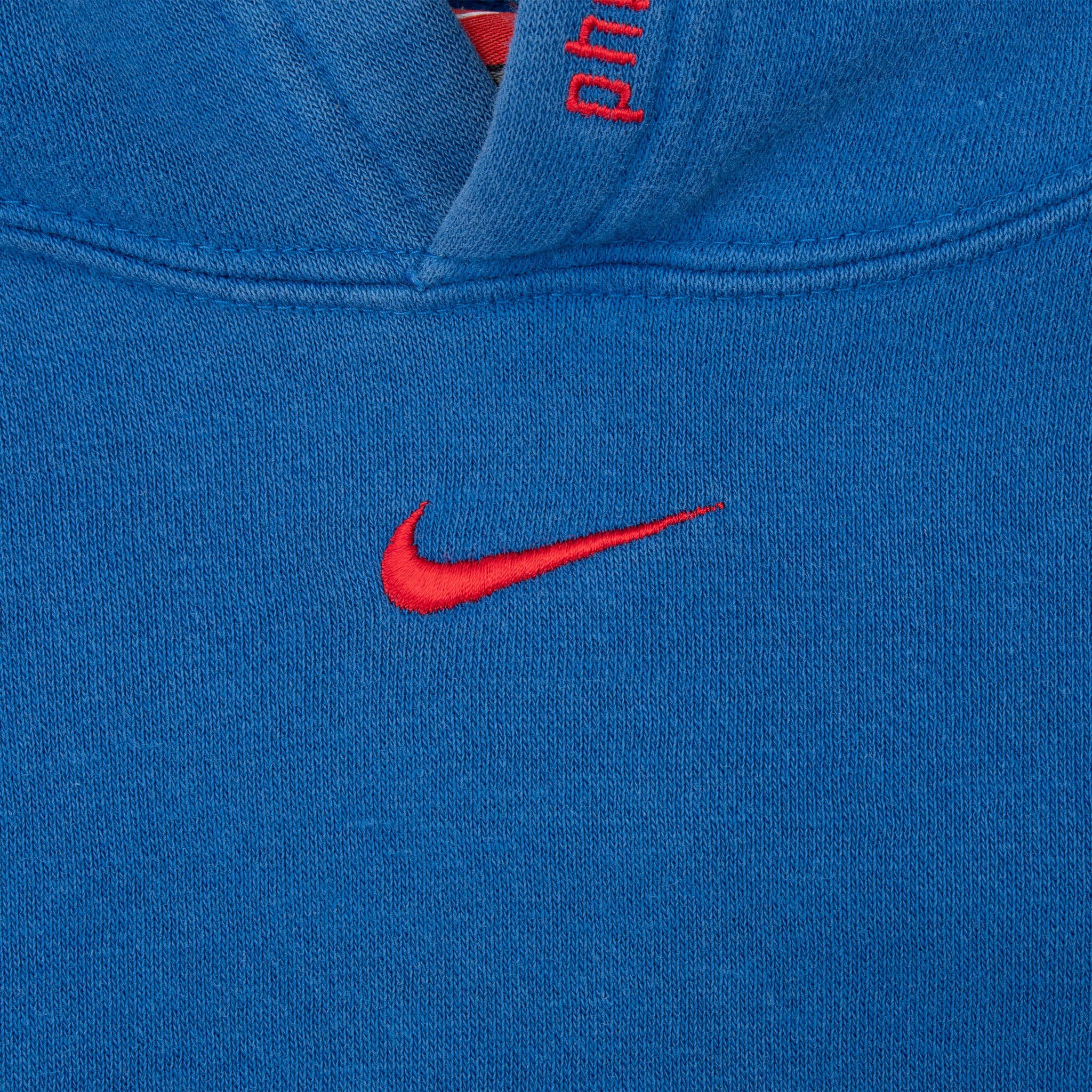 Red Nike Swoosh embroidery below the neckline of blue Sixers hoodie