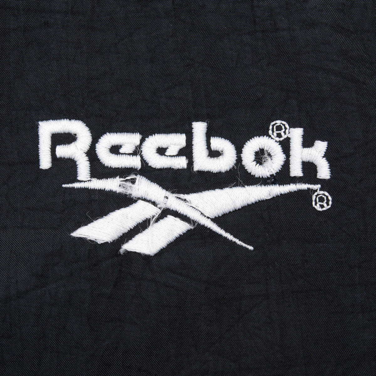 Close-up of white Reebok logo embroidery on black chest panel