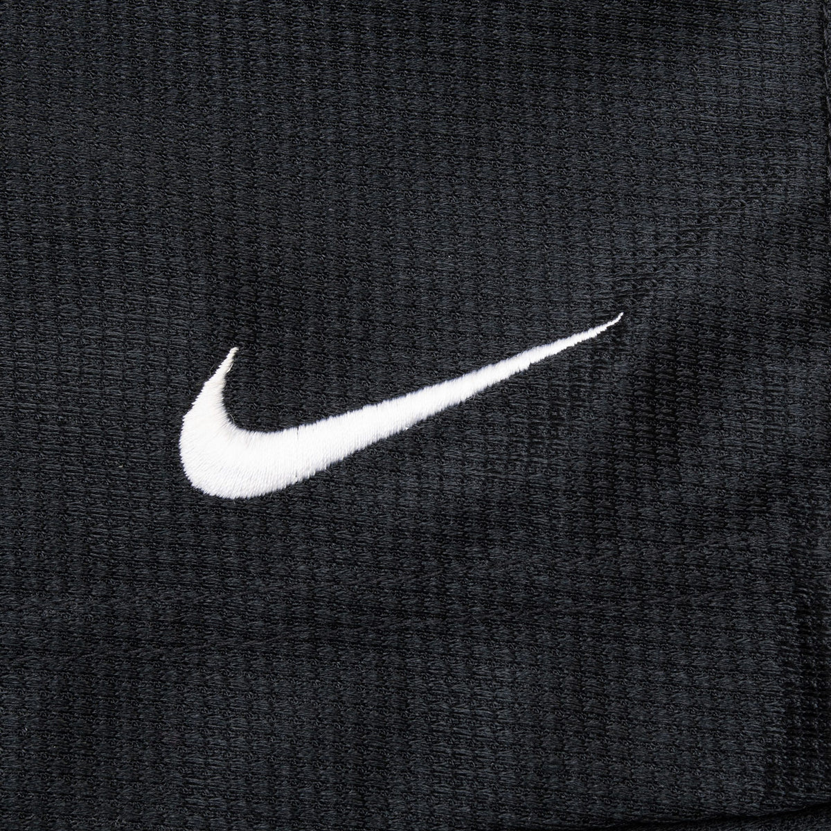 Close-up of white embroidered Nike Swoosh on textured black fabric
