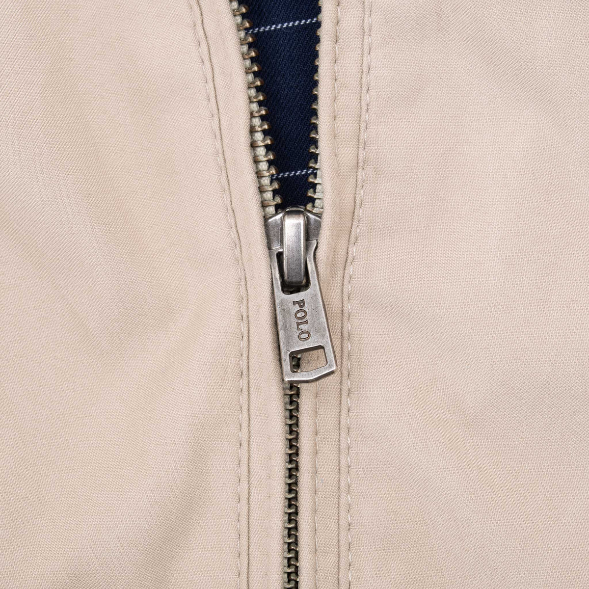 Close-up of metal Polo zipper pull and beige jacket fabric