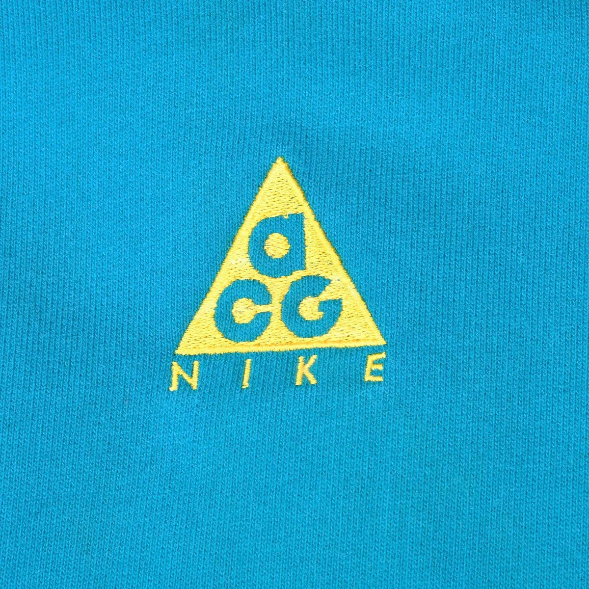 Close-up of yellow Nike ACG triangle logo embroidered on teal blue fabric