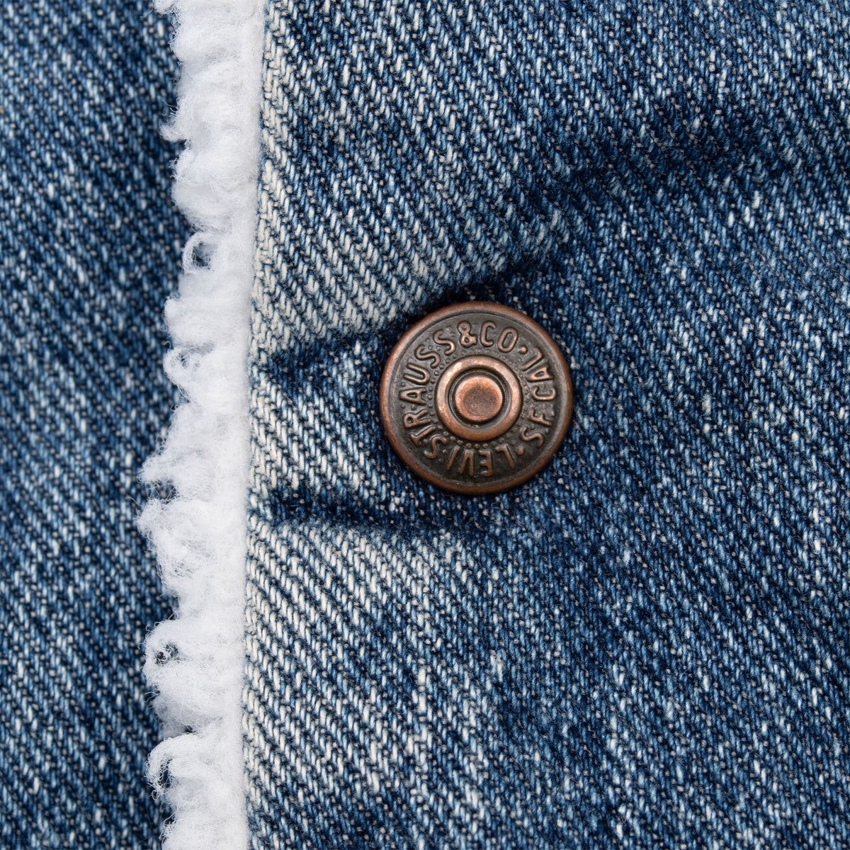Close-up of Levi Strauss metal button and white sherpa trim on blue denim