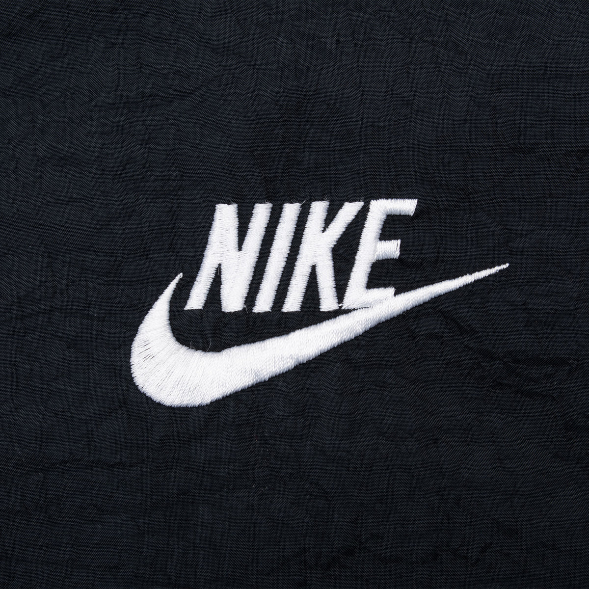 Close-up of white Nike and Swoosh embroidery on black jacket fabric