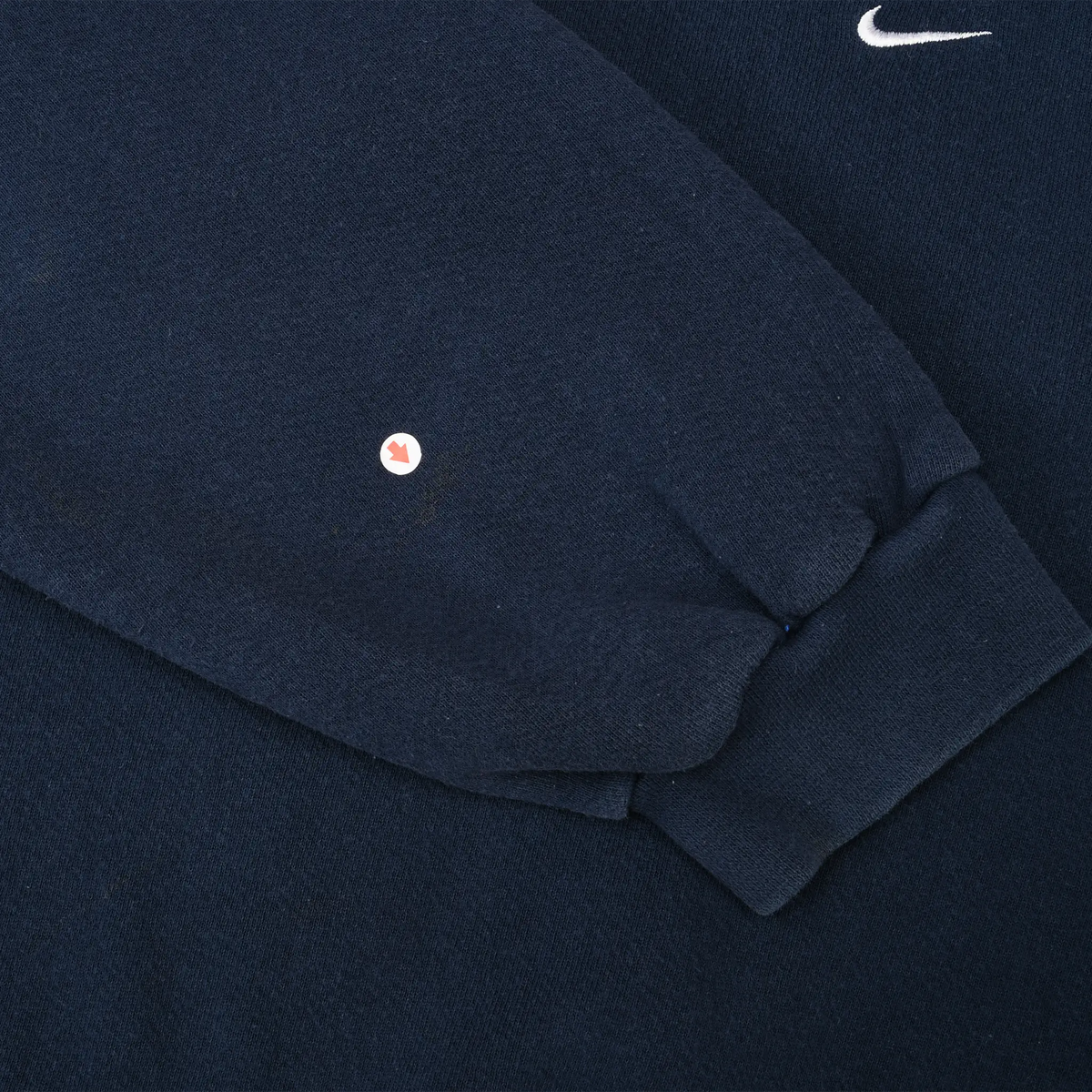 Close-up of navy blue sweatshirt sleeve showing a small hole near the ribbed cuff