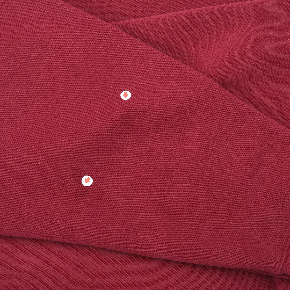 Close-up of burgundy sleeve fabric with two small areas highlighted by arrow markers