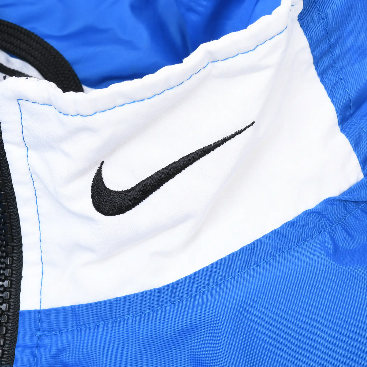 Black Nike Swoosh embroidery on white collar panel of blue windbreaker jacket