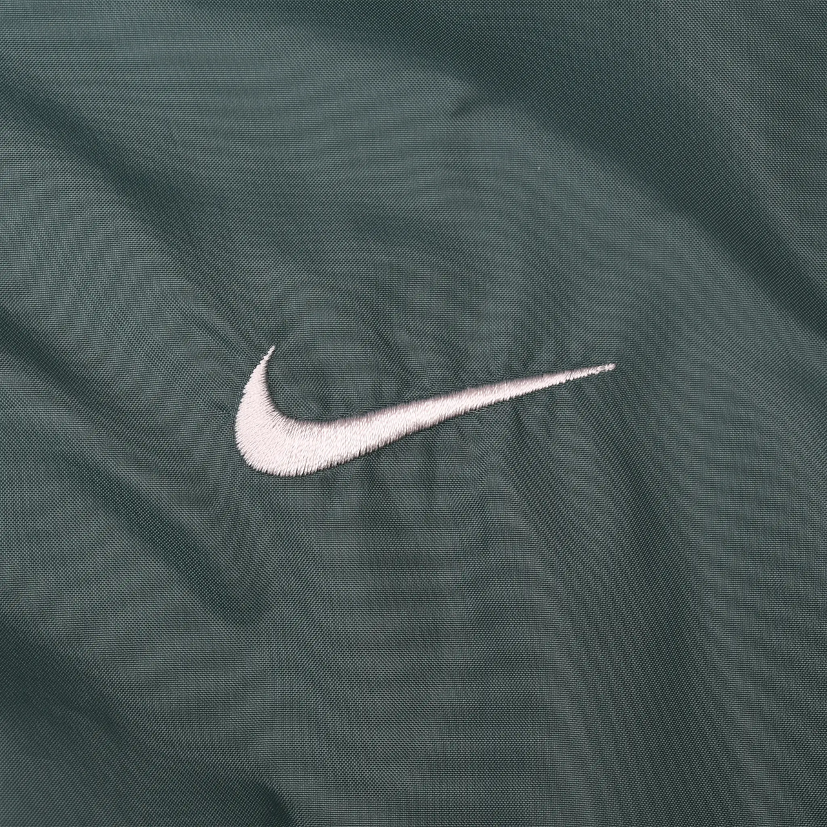 Close-up of white Nike Swoosh embroidery on green fabric