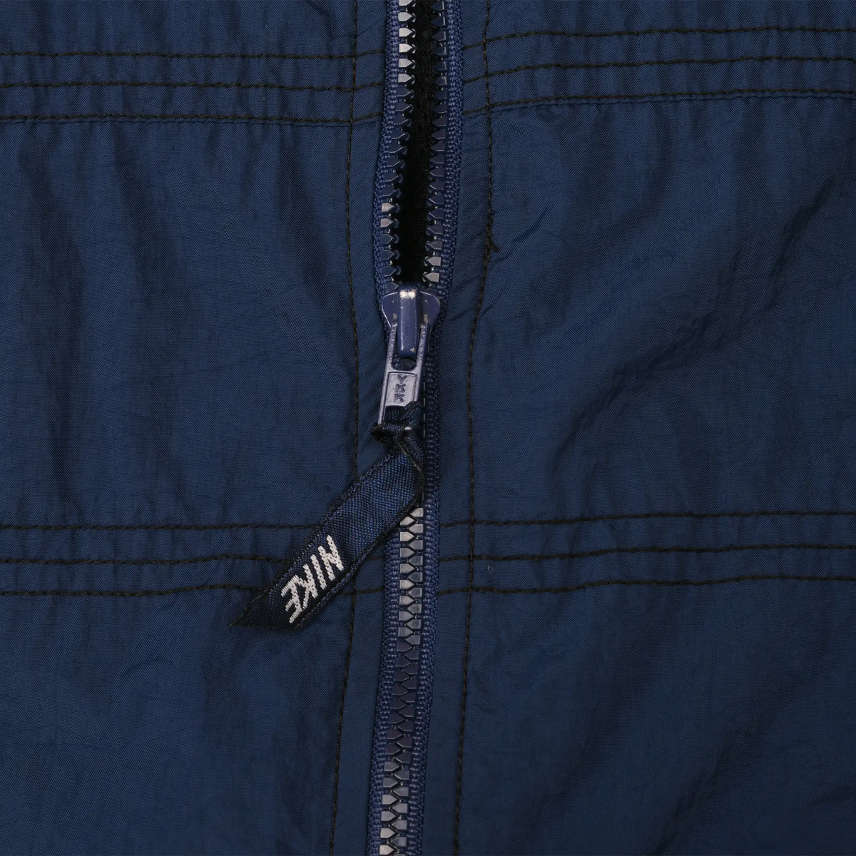 Close-up of navy jacket front zipper with black Nike logo pull tab