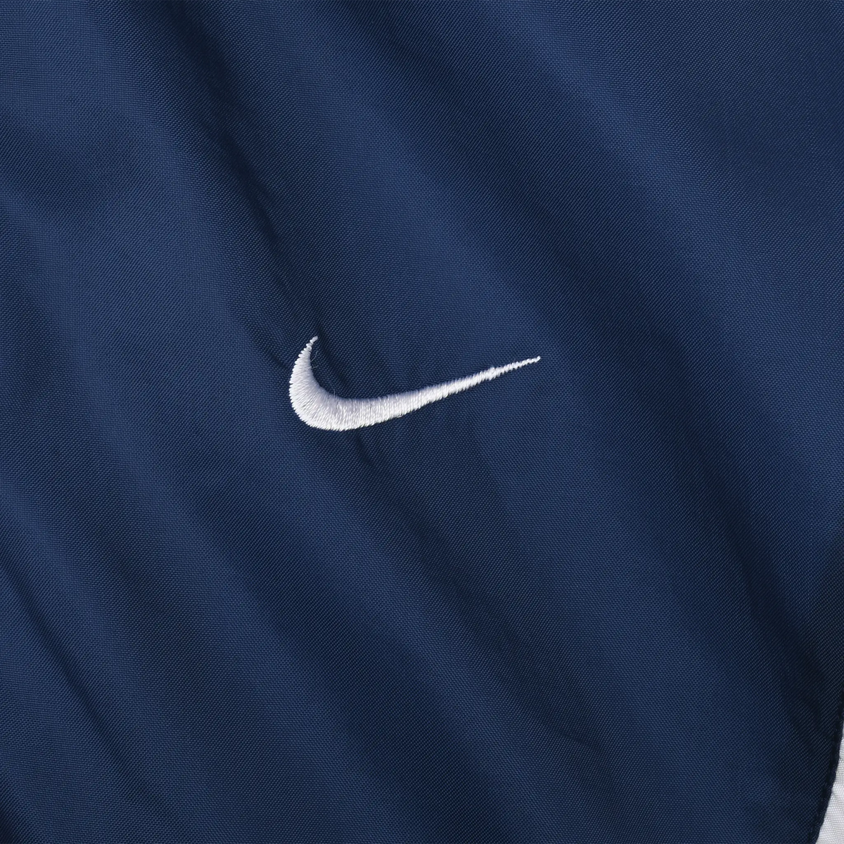 Close-up of white embroidered Nike Swoosh on navy blue jacket fabric