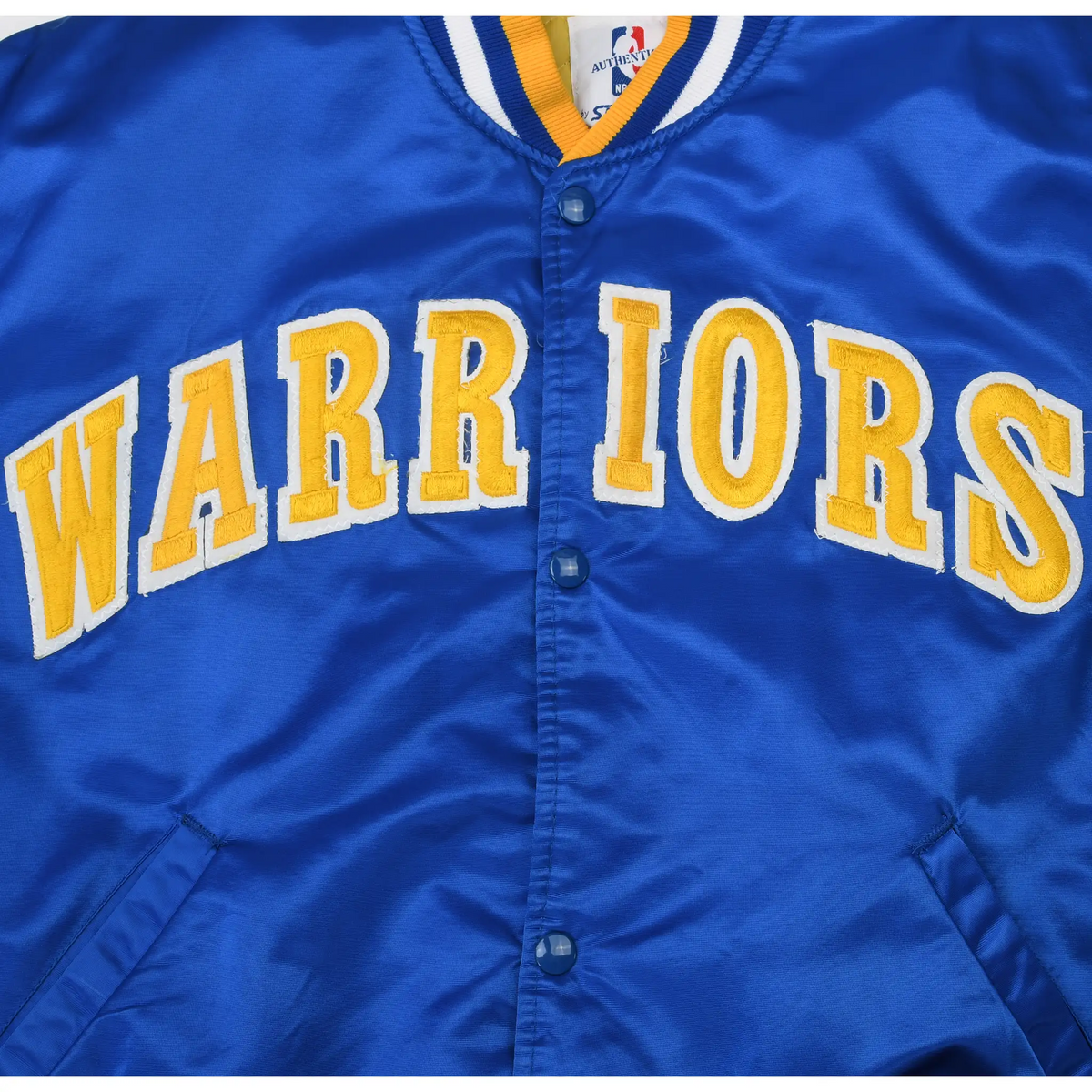 Close-up of gold and white Warriors lettering and snap closures on blue jacket front