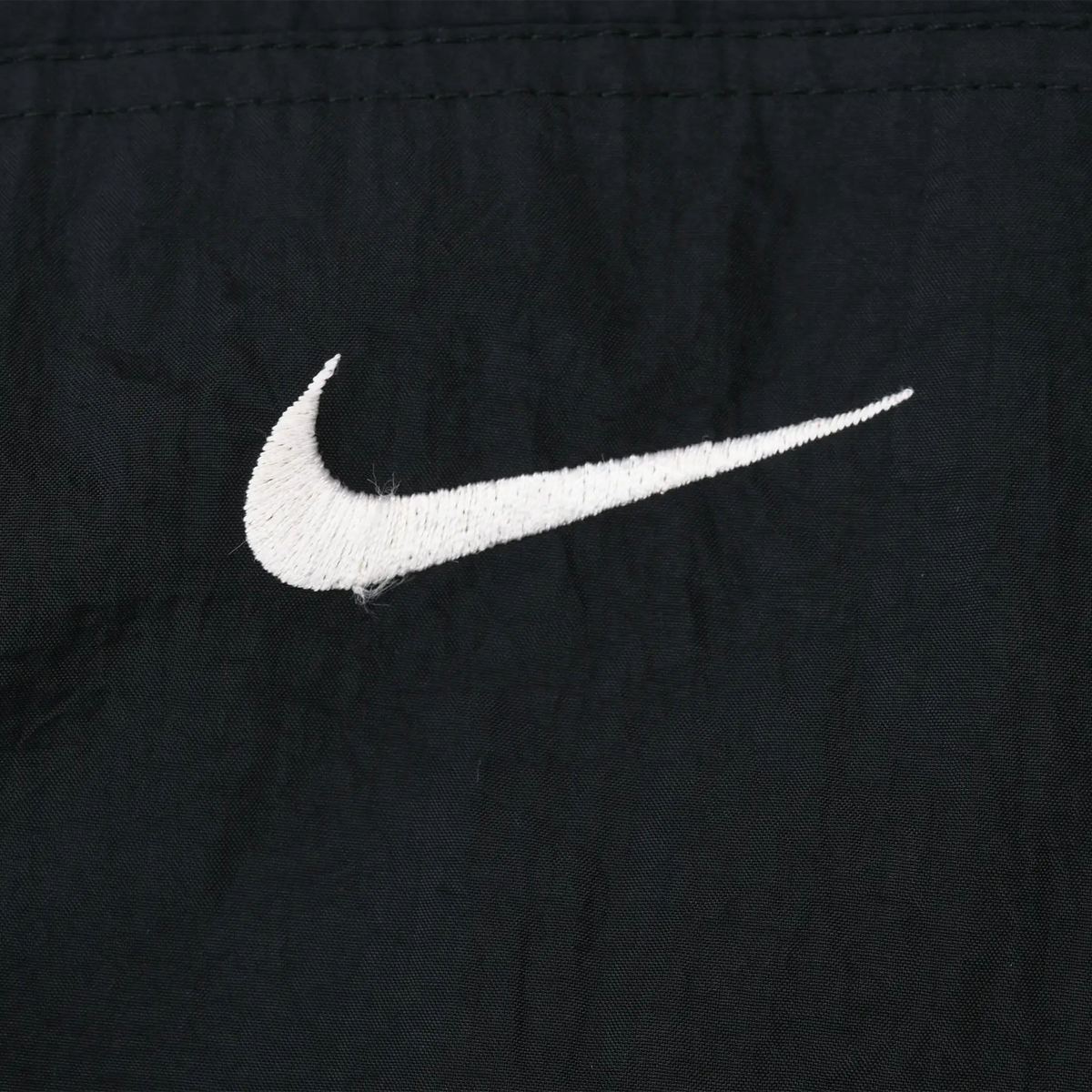Close-up of white embroidered Nike Swoosh on black windbreaker fabric
