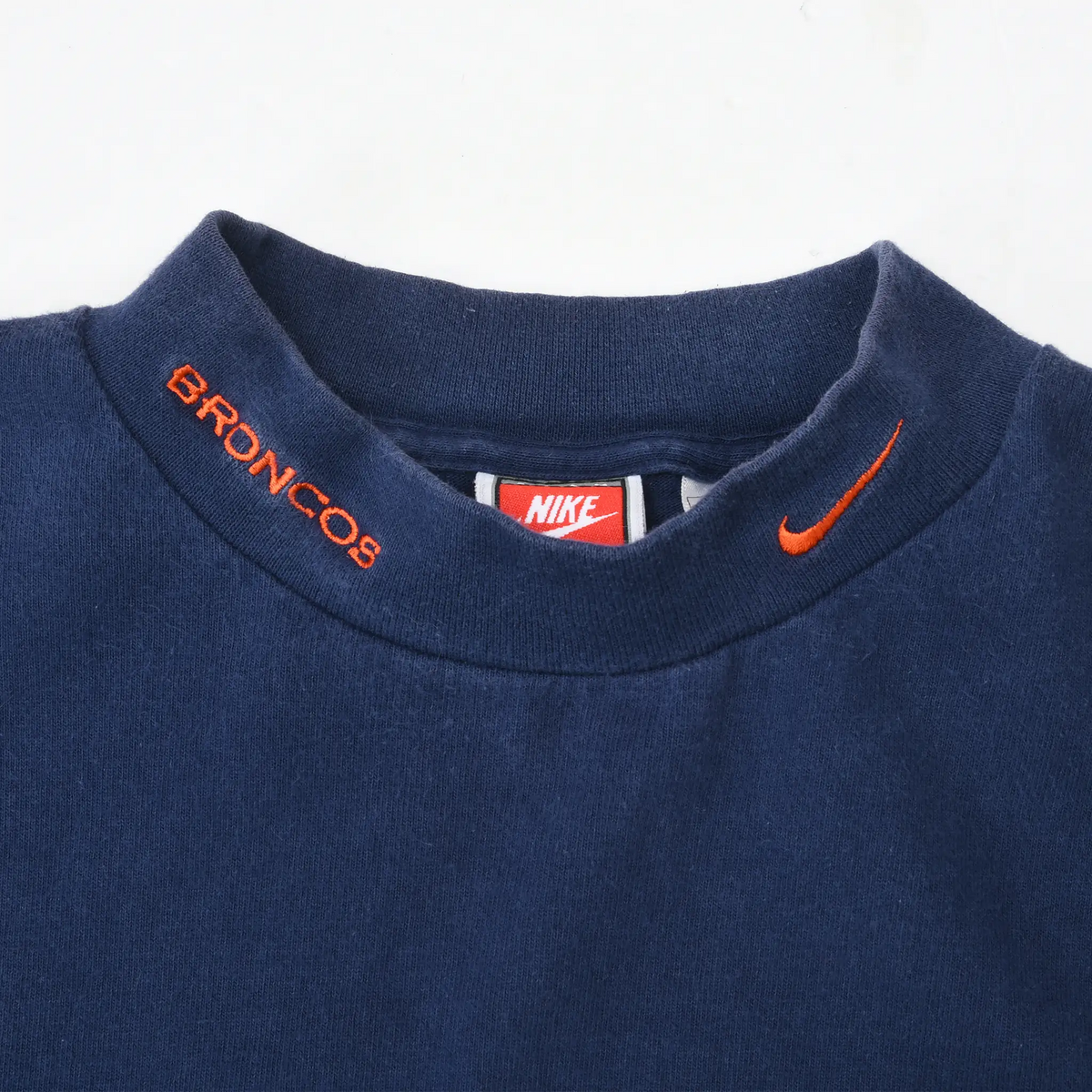 Close-up of navy turtleneck collar with orange Broncos lettering and Nike Swoosh embroidery