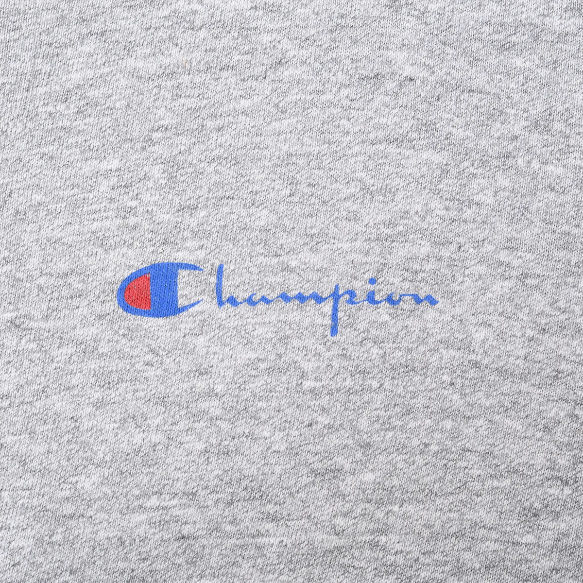 Close-up of the small blue and red Champion chest logo on heather gray fabric