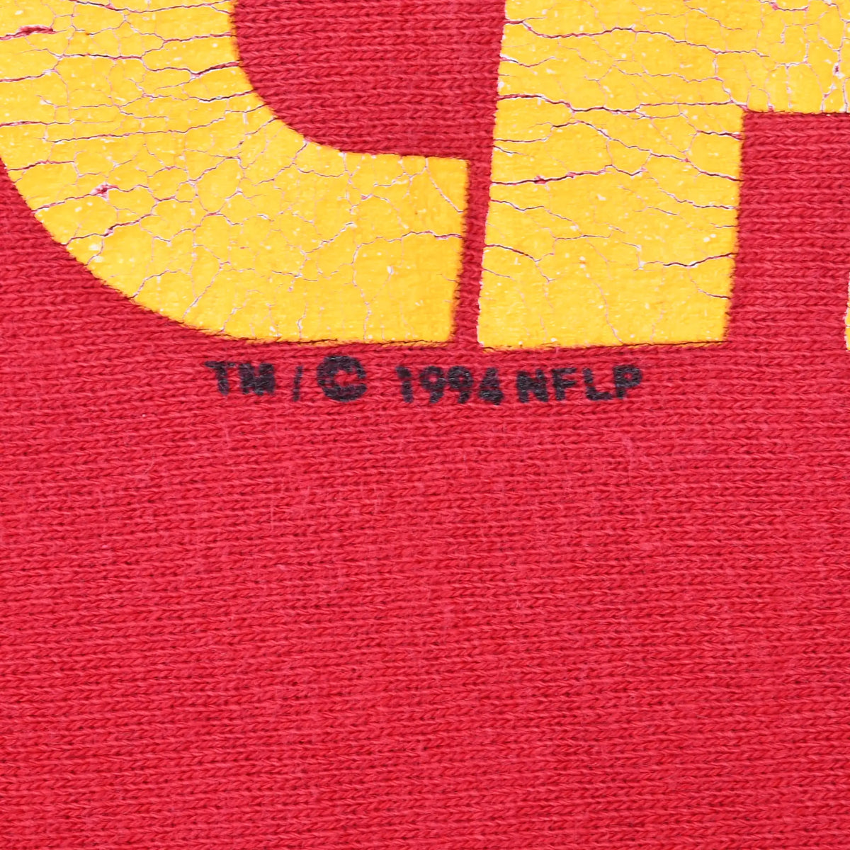 Close-up of cracked yellow print and 1994 NFLP copyright mark on red fabric