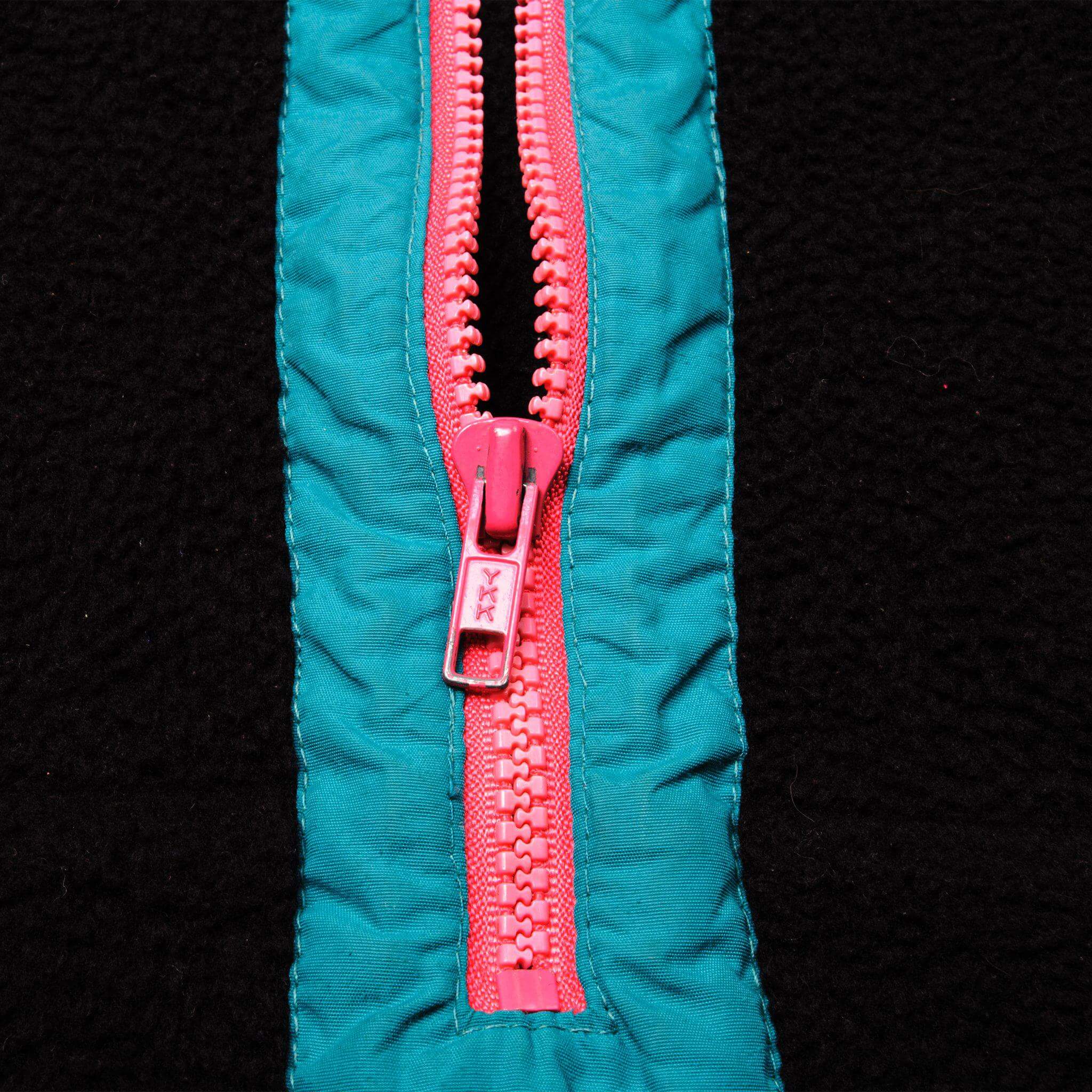 Close-up of pink YKK half zipper with gathered teal trim on black fabric