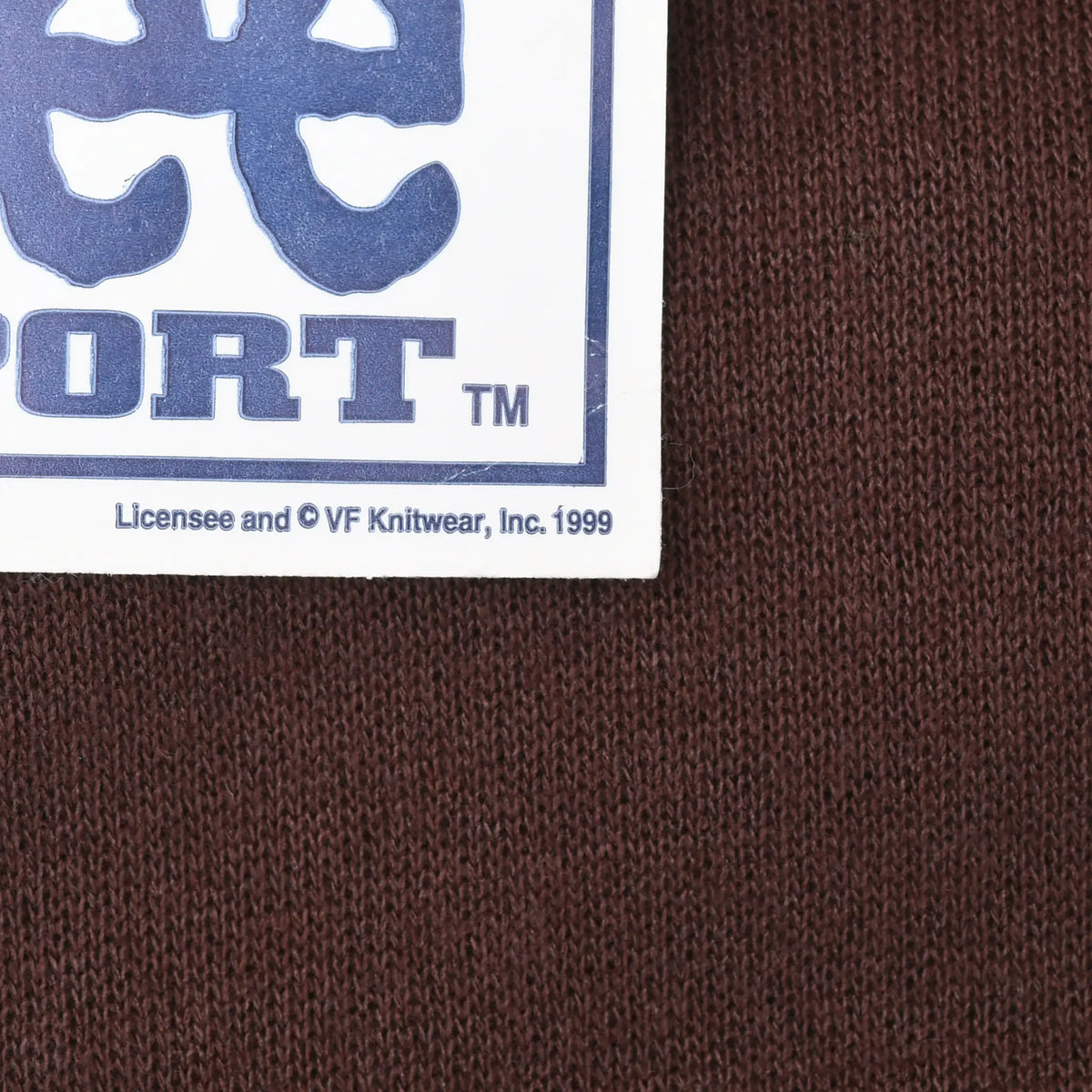 Close-up of brown sweatshirt fabric and Lee Sport hangtag with 1999 licensee text