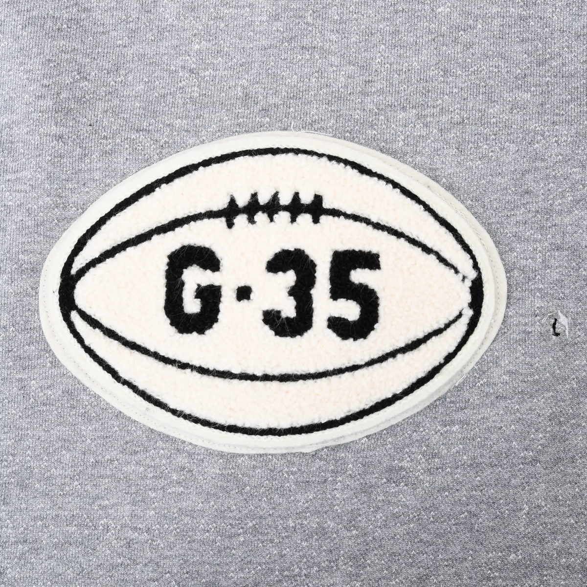 Close-up of cream football-shaped G-35 chest patch on grey sweatshirt