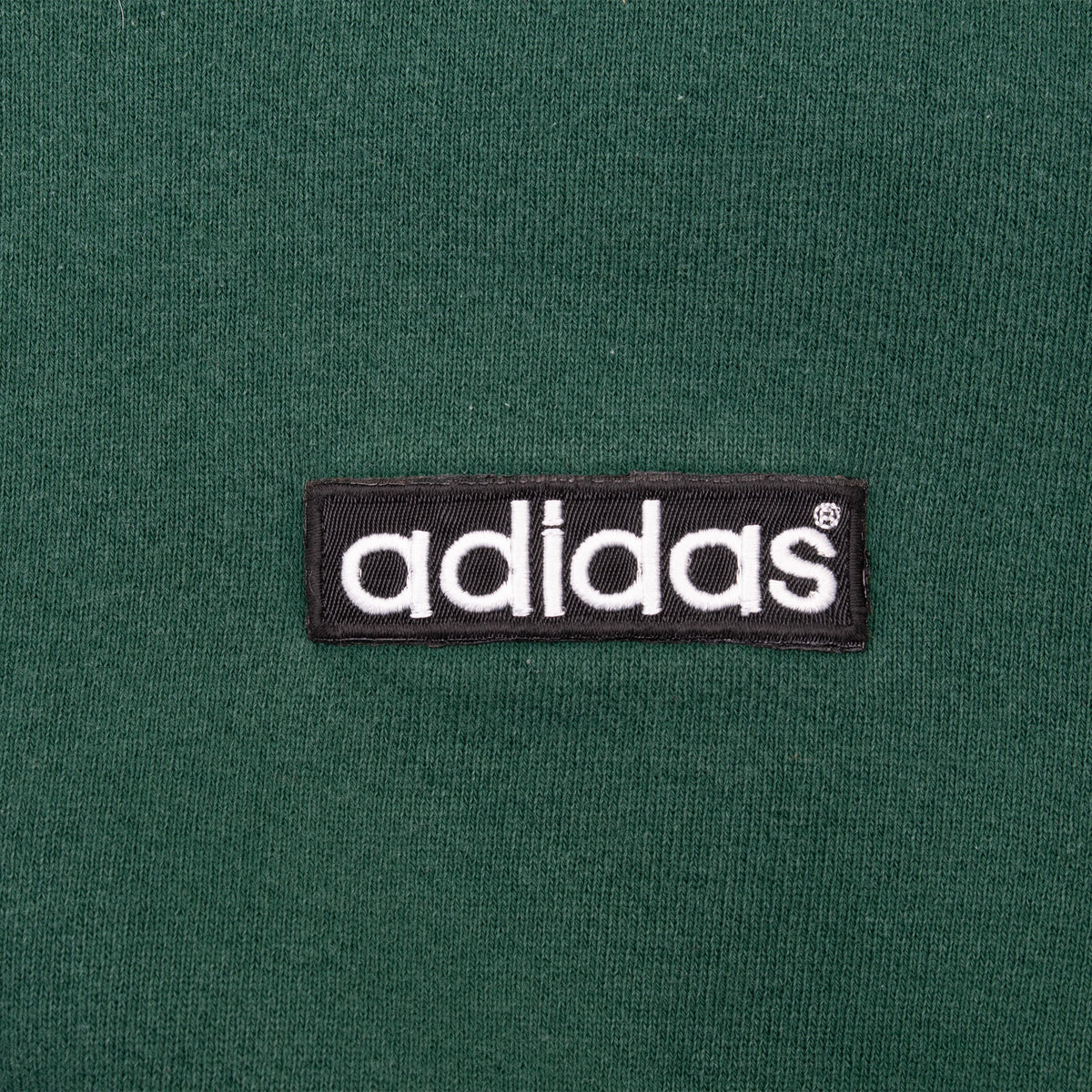 Close-up of black and white Adidas logo patch on green sweatshirt