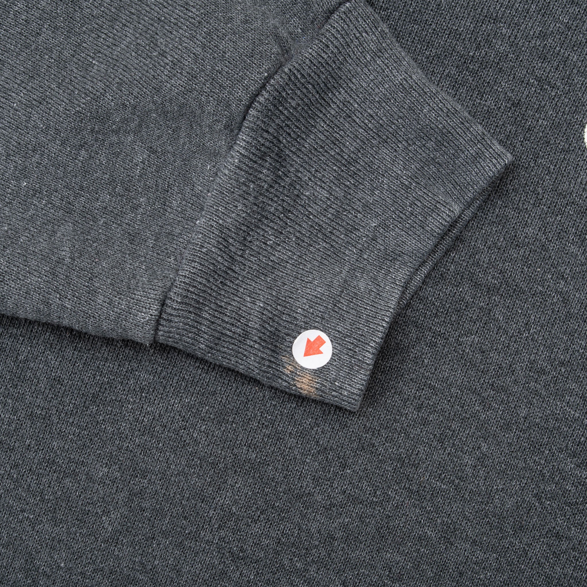 Close-up of ribbed grey sleeve cuff with small discolored spot marked by an arrow