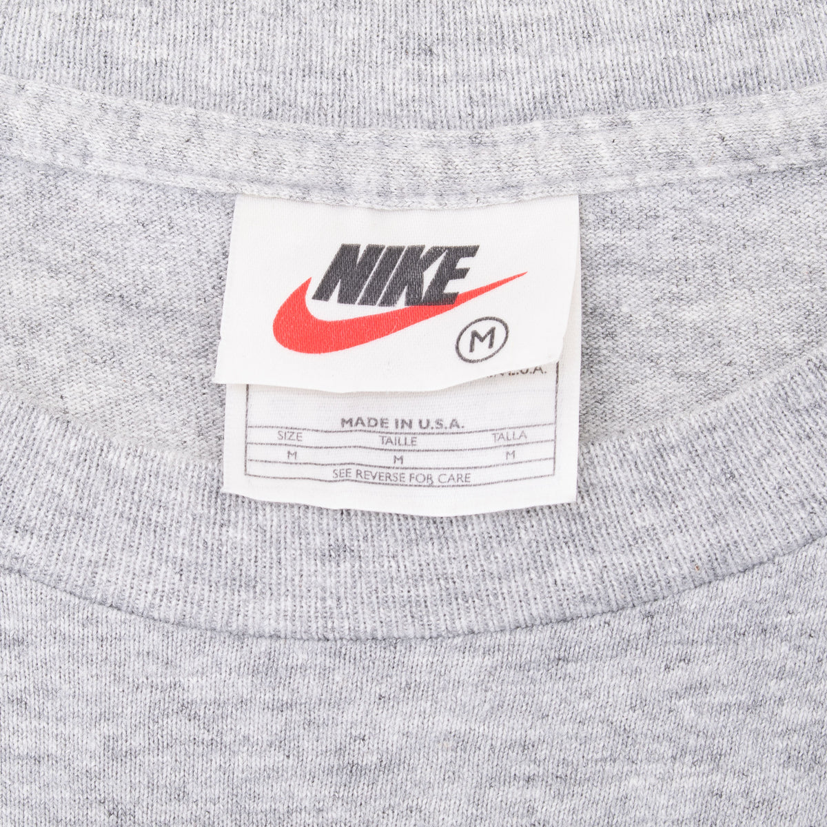 Nike neck tag detail on grey T-shirt showing medium size and Made in USA text