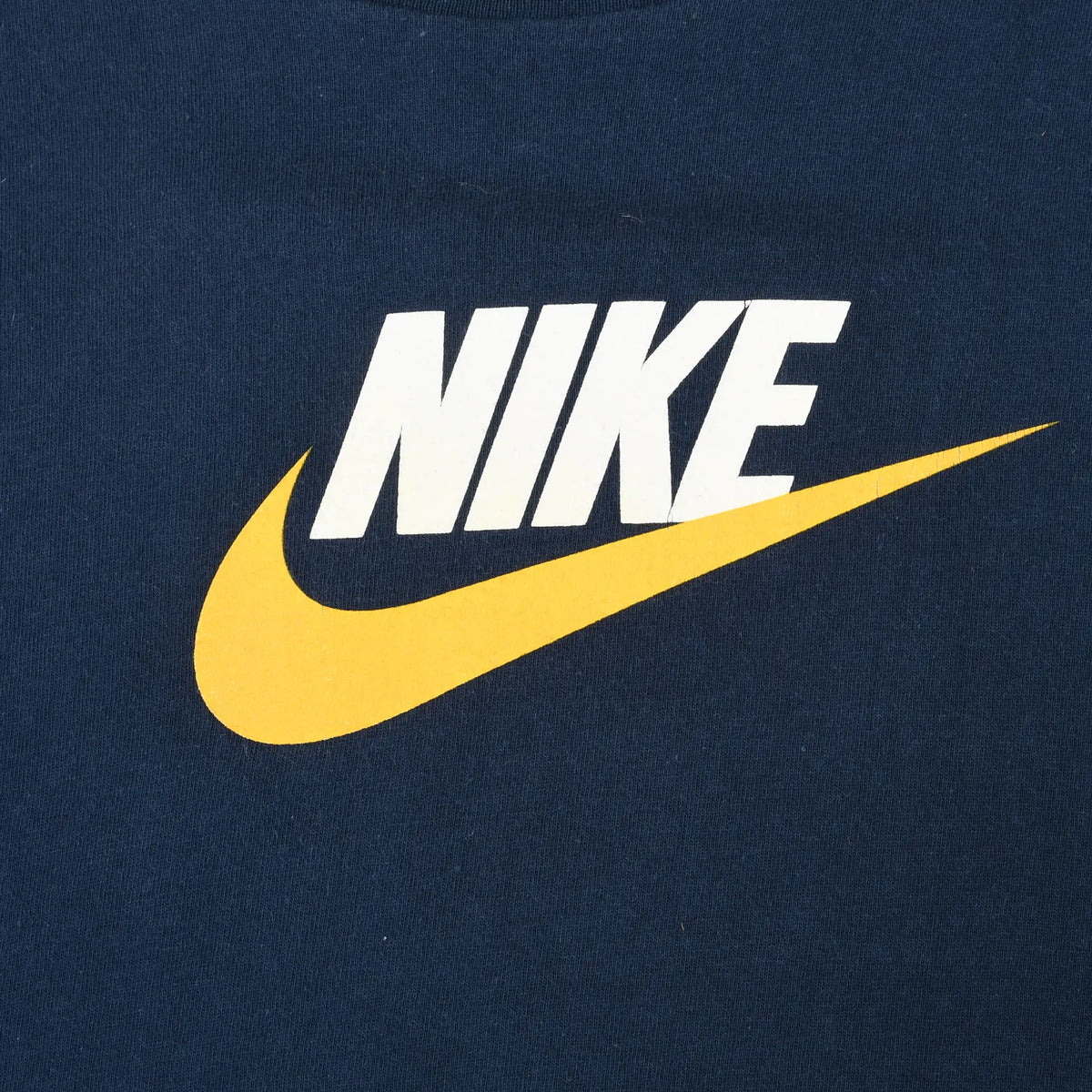 Close-up of white Nike spellout print and yellow Swoosh on navy fabric