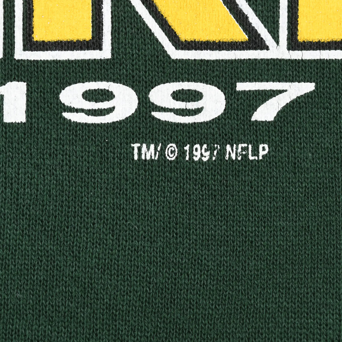 Close-up of white 1997 and TM copyright NFLP text printed on dark green sweatshirt fabric
